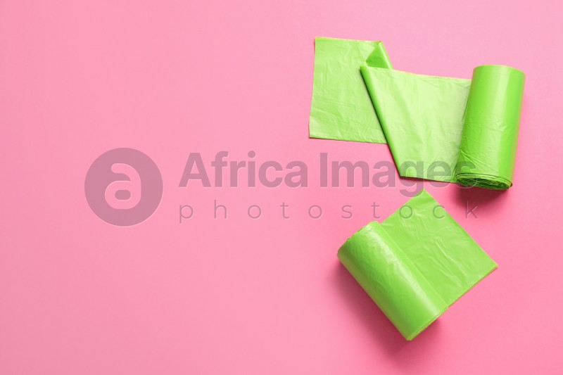 Photo of Rolls of green garbage bags on pink background, flat lay. Space for text