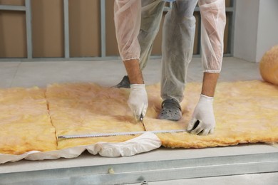 Worker measuring and cutting insulation material indoors, closeup. Space for text
