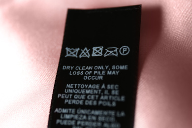 Clothing label with care symbols on pink silk shirt, closeup view