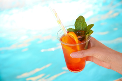 Woman with glass of refreshing drink near swimming pool, closeup. Space for text