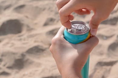 Woman opening aluminum can with beverage on sand, closeup. Space for text