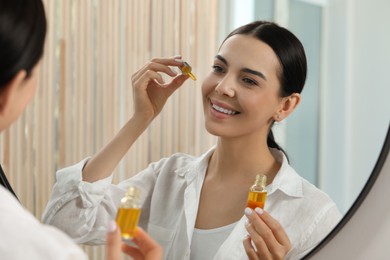 Young woman with bottle of essential oil near mirror indoors