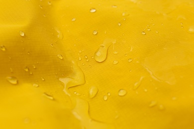 Yellow waterproof fabric with water drops as background, closeup