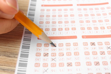 Woman filling out lottery ticket with pencil on wooden table, closeup. Space for text