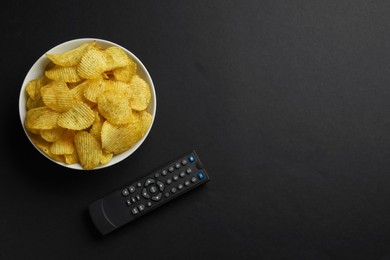 Modern tv remote control and chips on black background, flat lay. Space for text