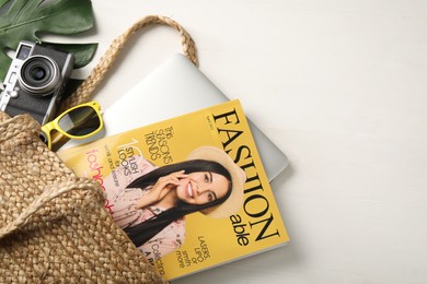Bag with fashion magazine, laptop and camera on white wooden table, above view. Space for text