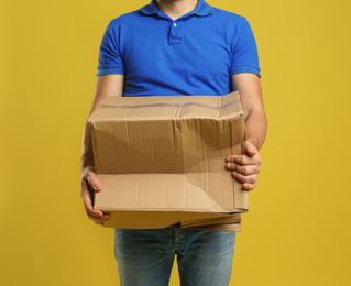 Courier with damaged cardboard box on yellow background, closeup. Poor quality delivery service