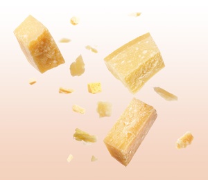 Pieces of delicious parmesan cheese flying on color background