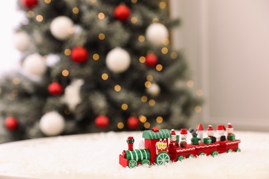 Bright toy train on artificial snow in room with Christmas tree