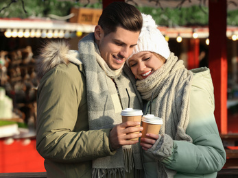 Happy couple in warm clothes with drinks at winter fair. Christmas season
