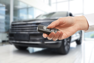 Image of Car buying. Woman holding key against blurred automobile, closeup