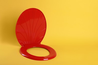 New red plastic toilet seat on yellow background, space for text
