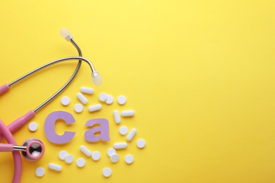 Photo of Stethoscope, pills and calcium symbol made of purple letters on yellow background, flat lay. Space for text