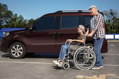 Senior man with boy in wheelchair near van on car parking