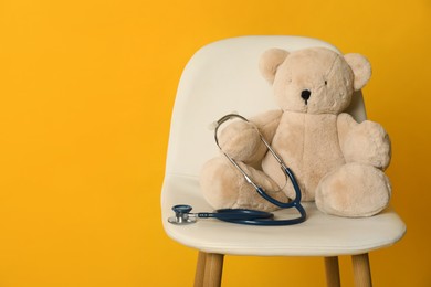 Teddy bear with stethoscope on chair against yellow background, space for text. Pediatrician practice