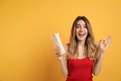 Excited young woman with delicious shawarma on yellow background, space for text