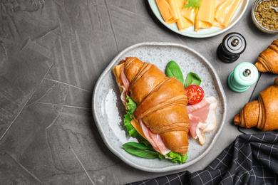 Flat lay composition with tasty croissant sandwich on grey table, space for text