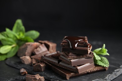 Tasty chocolate pieces with syrup and mint on black table, closeup