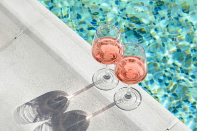 Photo of Glasses of tasty rose wine on swimming pool edge, space for text