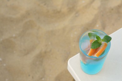 Glass of refreshing drink with grapefruit and mint on white table at beach, above view. Space for text