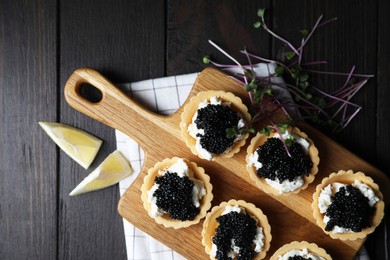 Photo of Board of delicious tartlets with black caviar and cream cheese on wooden table, top view