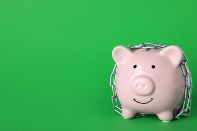 Piggy bank  with steel chain on green background, space for text. Money safety concept