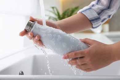Photo of Woman washing thermo bottle in kitchen, closeup