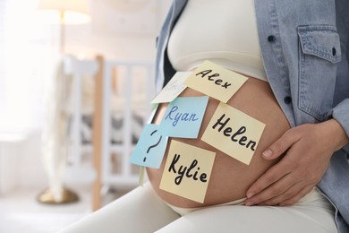 Pregnant woman with different baby names on belly at home, closeup. Space for text