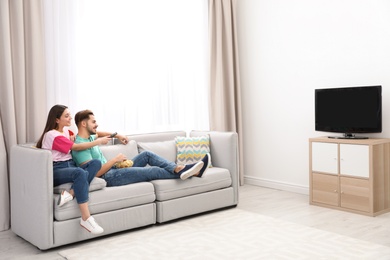 Photo of Couple with snack watching TV on sofa together at home. Space for text