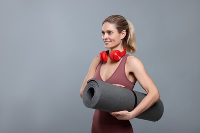 Photo of Sportswoman with headphones and fitness mat on grey background, space for text