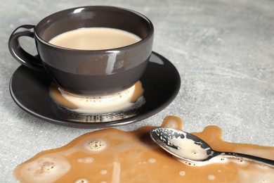 Cup, saucer and spoon near spilled coffee on grey table, closeup