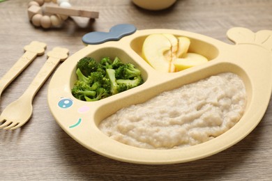 Photo of Plastic dishware with healthy baby food on wooden table, closeup