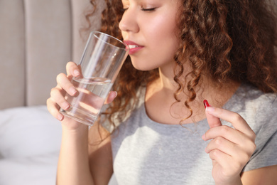 African-American woman with glass of water and vitamin pill at home, closeup
