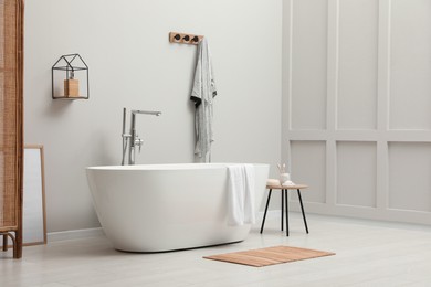 Modern ceramic bathtub with towel near white wall in room