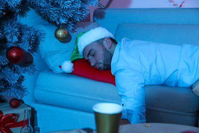 Photo of Drunk man wearing Santa hat sleeping on sofa after New Year party