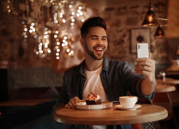 Photo of Young blogger taking selfie at table in cafe