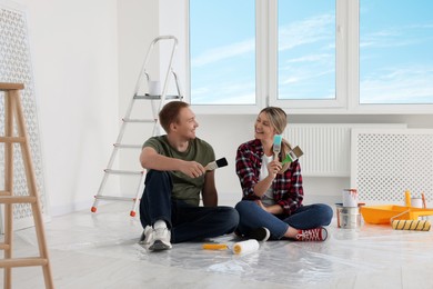 Happy couple with brushes and painting tools on floor in apartment during repair
