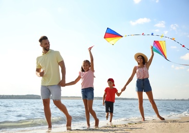 Happy parents and their children playing with kites on beach near sea. Spending time in nature