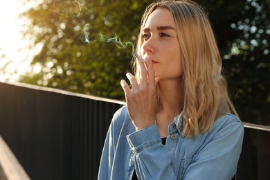 Young woman smoking cigarette outdoors, space for text