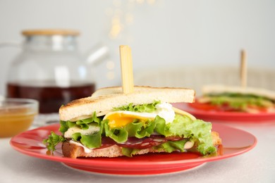 Photo of Delicious sandwich with vegetables, egg and salami on white table, closeup