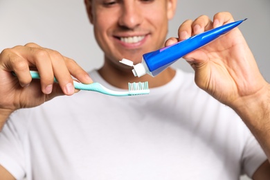 Man applying toothpaste on brush against light background, closeup