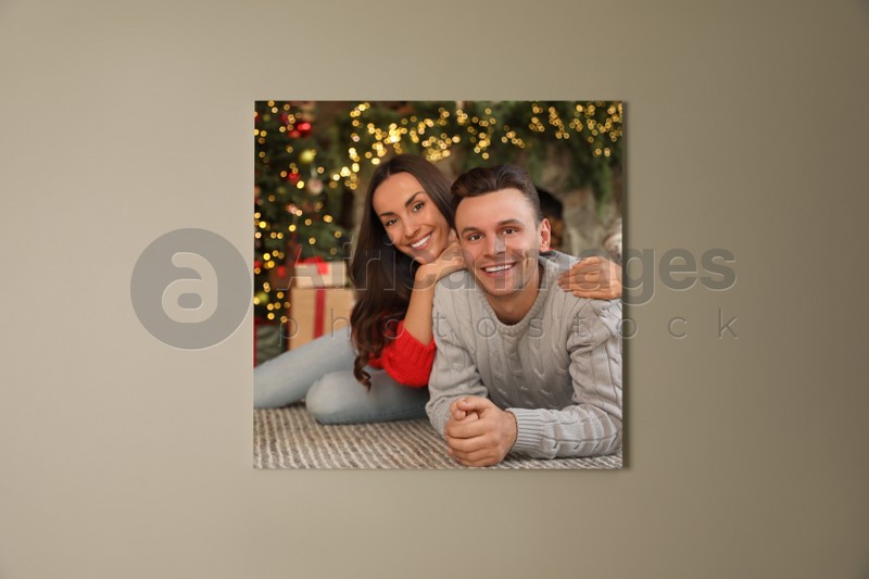 Canvas with printed photo of happy couple in room decorated for Christmas on beige wall