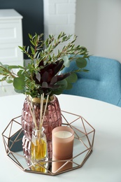 Beautiful bouquet with eucalyptus branches, candle and aromatic reed air freshener on white table indoors. Interior elements