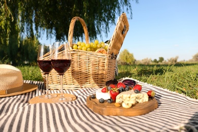 Photo of Red wine and different products for summer picnic served on blanket outdoors