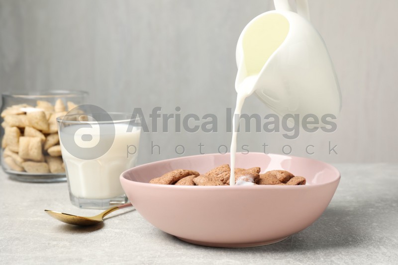 Pouring milk into bowl of tasty corn pads served for breakfast on light table