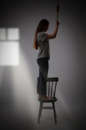 Depressed woman with rope noose standing on chair in room