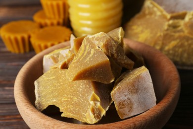Photo of Bowl with natural beeswax blocks on wooden table, closeup
