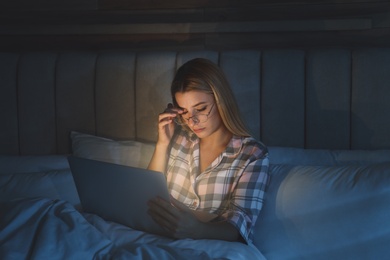 Photo of Young woman using laptop in bed at night. Sleeping disorder problem