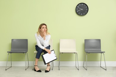 Young woman with clipboard waiting for job interview indoors