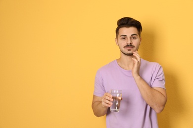 Young man with sensitive teeth and glass of water on color background. Space for text